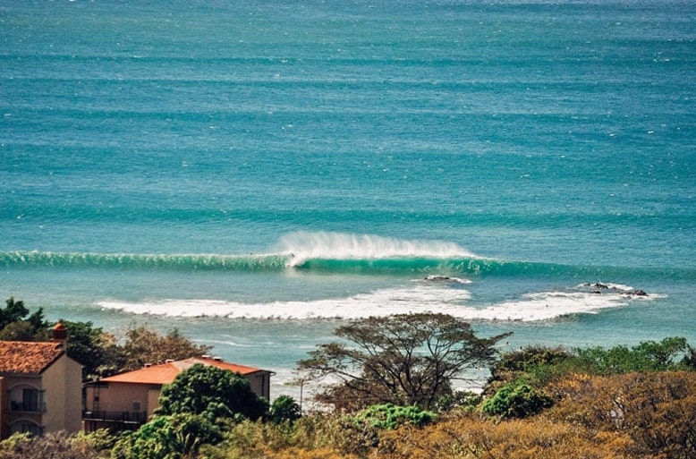 Perfect surfing wave rolling in at Tamarindo Beach Costa Rica, with coastal homes in the foreground