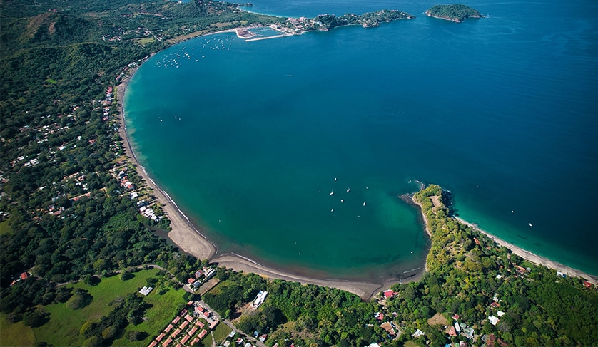 Aerial view of the bay of Playa Flamingo, Costa Rica, highlighting the lush green vegetation, wide beach and crystal blue water