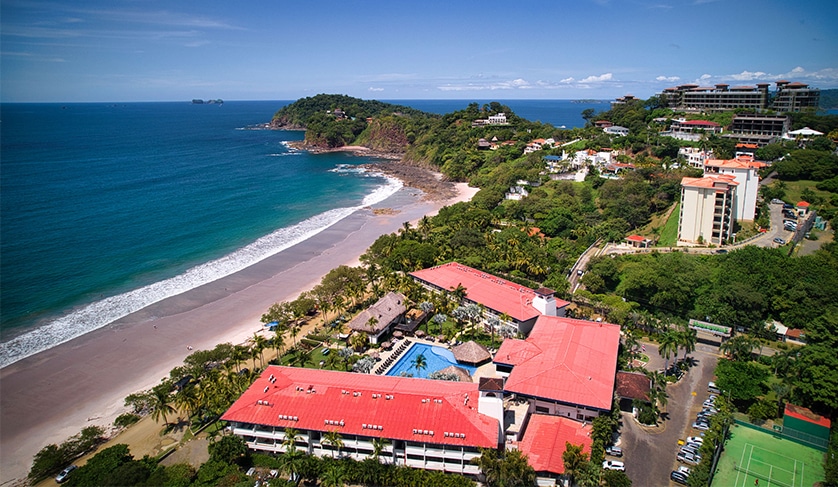 Beachfront resorts in Playa Flamingo, Costa Rica, with a dark sandy beach and crystal clear waters, and a panoramic view of the coast.